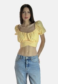 Top corto giallo a quadretti con maniche a sbuffo e dettaglio frontale arricciato, abbinato a pantaloni corti in denim blu a vita alta.