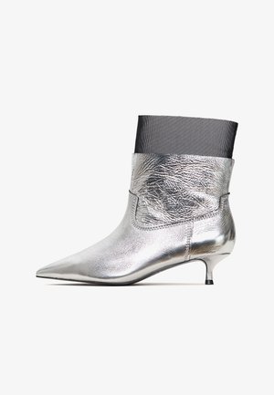 Stříbrné kovové kotníkové boty s špičatou špičkou, s texturovaným koženým povrchem a černým textilním vrchním lemem. Design s kitten heel.