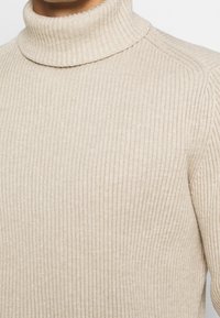 Maglione a dolcevita beige a costine con una vestibilità aderente, caratterizzato da un collo alto e un tessuto testurizzato, adatto per essere indossato a strati o da solo.