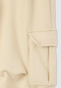 Jasnobeżowy materiał o gładkiej teksturze, z półdługością mankietu, który ma zagięty brzeg i akcenty w postaci stębnowania.