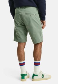 Lys grønne shorts med rett passform, baklommepåknapper og glidelåslomme. Båret med hvite joggesko og ribbestrikkede sokker med røde og blå striper.