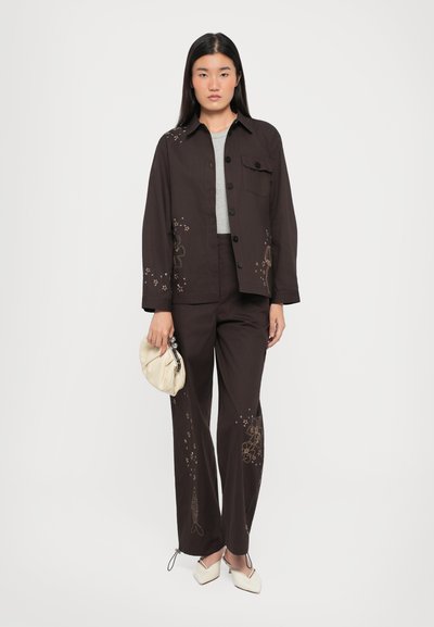 Dark brown embroidered jacket with matching pants, featuring floral and fish patterns. Paired with a light gray top and cream clutch.