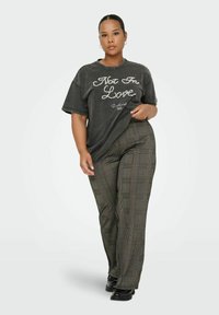 T-shirt graphique gris avec le texte "Not In Love" en blanc, associé à un pantalon à carreaux taille haute dans des tonalités de vert, marron et orange.