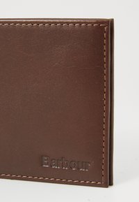 Brown leather wallet corner with visible stitching and embossed Barbour brand name on a white background.
