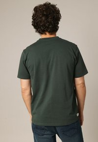 Camiseta de algodón verde con mangas cortas y un cuello redondo. Diseño simple sin patrones ni logotipos visibles. Corte estándar.