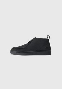 Bottines en suède noir à lacets avec tirant et semelle texturée, présentant un petit logo de crocodile embossé sur le côté.