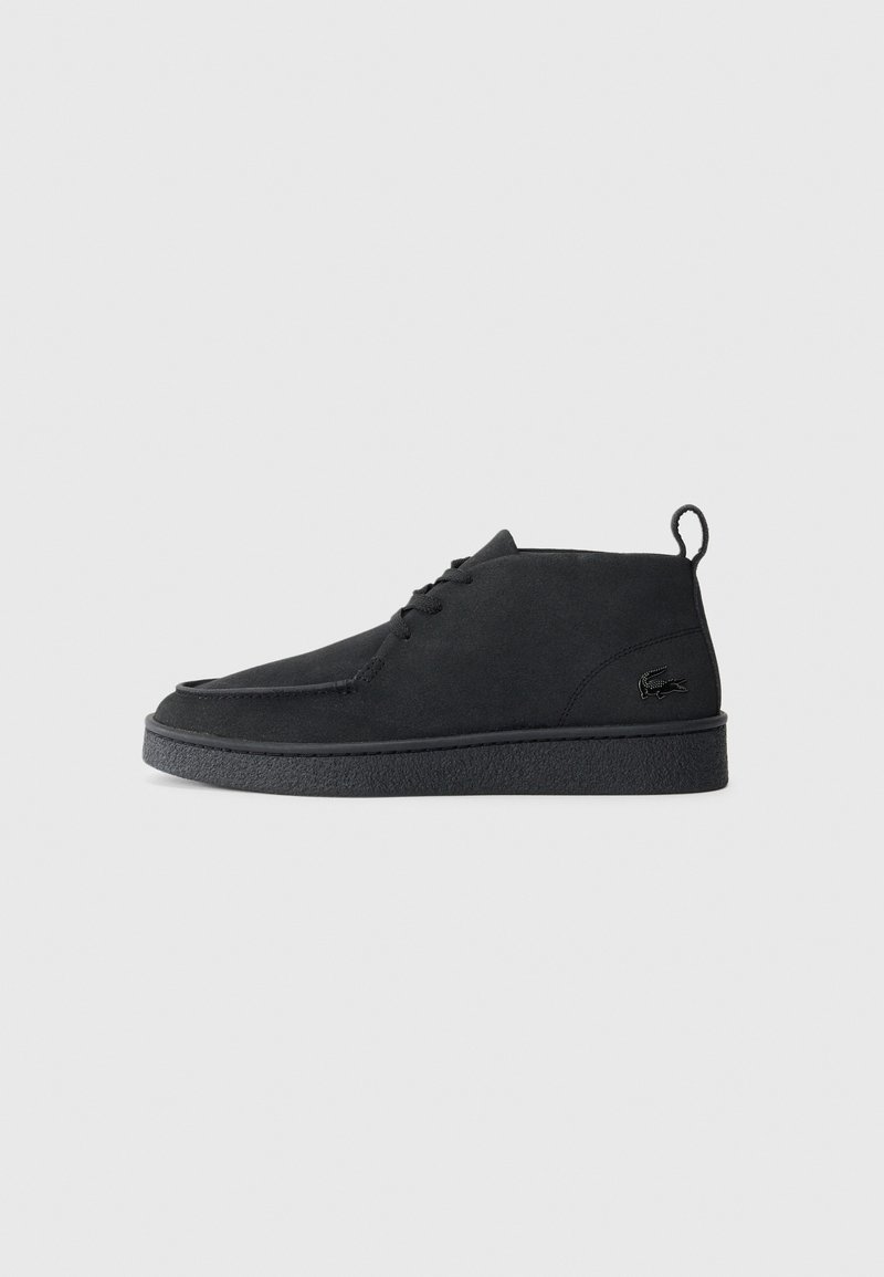 Bottines en suède noir à lacets avec tirant et semelle texturée, présentant un petit logo de crocodile embossé sur le côté.