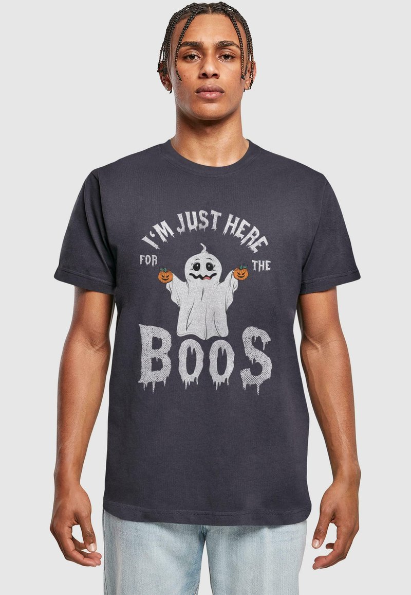 Svart bomullströja med en spökgrafik och pumpor, text som säger "JAG ÄR BARA HÄR FÖR ATT DRICKA", och sliten stil på bokstäverna.