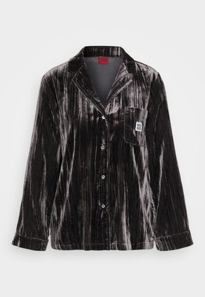 Musta samettinen pyjama-toppi, jossa on teksturoitu, uritettu muotoilu. Varustettu kaartuvalla kauluksella, kuudella napilla ja rintataskulla, jossa on logopatch.