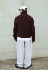 Bordo skraćeni sako s visokim ovratnikom, dugim rukavima i detaljima šivanja, uparen sa sivim hlačama širokih nogavica i crnom obućom.