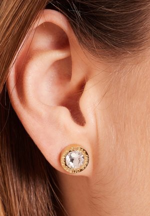 Gold stud earrings featuring a clear crystal center, with "GUESS" engraved around the edge. Designed for pierced ears.