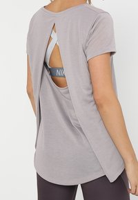 Top gris de manga corta con un diseño de espalda abierta, que revela un sujetador deportivo de color azul claro debajo. Tejido suave con un corte relajado.