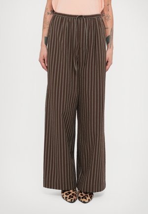 Brune bukser med vide ben og lodrette striber samt snøre i taljen. Glat tekstur, afslappet pasform, kombineret med sko med leopardprint.