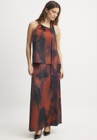 A halter neck top and matching long skirt in a flowing fabric featuring a red and dark blue watercolor pattern with a tied detailing.