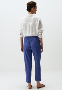 Witte linnen blouse met opgerolde mouwen, gecombineerd met blauwe broeken met elastische taille en achterzakken. Eenvoudig, relaxte pasvorm ontwerp.