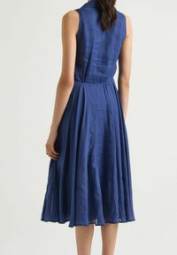 Navyblaues ärmelloses Kleid mit Kragen, tailliertem Bund und fließendem Rock in leichter Textur, der bis zur Mitte der Waden reicht.