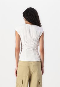 Haut blanc ajusté avec des manches courtes et des détails froncés à l'arrière, associé à un pantalon cargo beige clair doté de grandes poches.