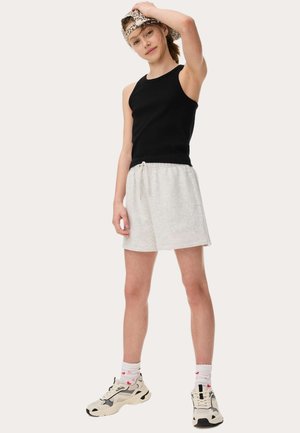 Haut sans manches noir, short en jersey gris avec ceinture ajustable, et casquette à motifs. Chaussures de sport avec accents noirs et beiges, et chaussettes blanches.