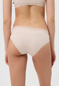 Beige gerippte Baumwoll-Hipster-Slips mit zarter Spitze am Bund und an den Beinausschnitten. Weiche Textur, nahtloses Design.