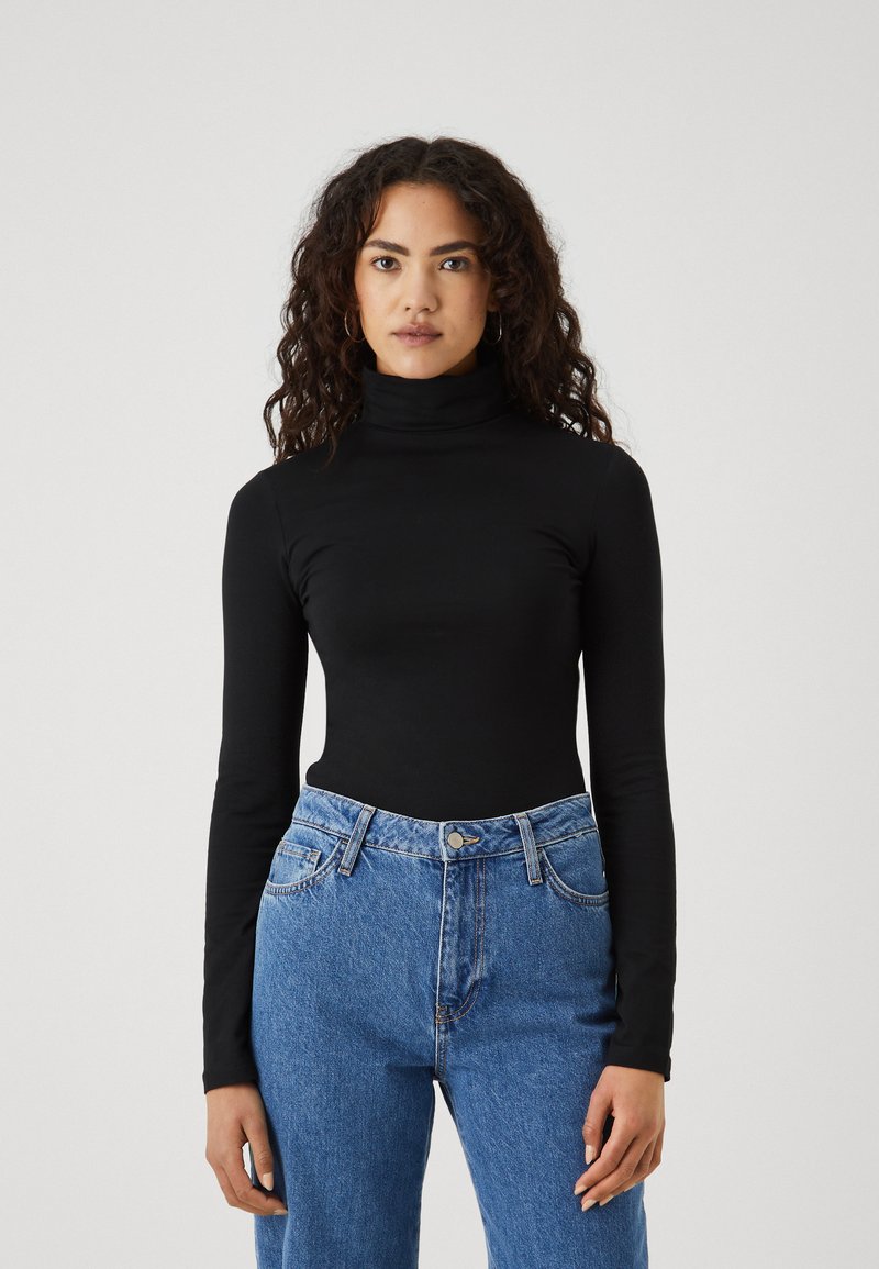 Zwarte turtleneck gemaakt van stretchstof met lange mouwen, gecombineerd met een hoge taille blauwe denim jeans met een knoopsluiting en vijf zakken.