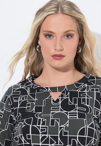 Musta ja harmaa yläosa, jossa on geometrinen valkoinen kuvio, pyöreä pääntie avoilta yksityiskohdilta sekä sileä ja joustava kankaan rakenne.