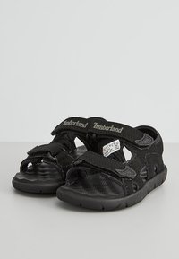 Sandali neri con cinturini in tessuto, chiusure a strappo, soletta testurizzata e suole in gomma. Logo Timberland sui cinturini. Vestibilità regolabile.