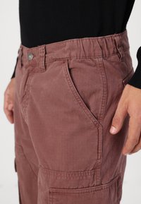 Küljepockets ja elastne vöökoht mugavuse tagamiseks, valmistatud tekstuurses kangas, tolmunud roosa värviga.