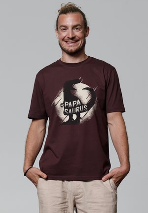 Bordeauxkleurig katoenen T-shirt met een dinosaurusschrift en de tekst "PAPA SAURUS" in het wit. Korte mouwen en een ronde halsontwerp.