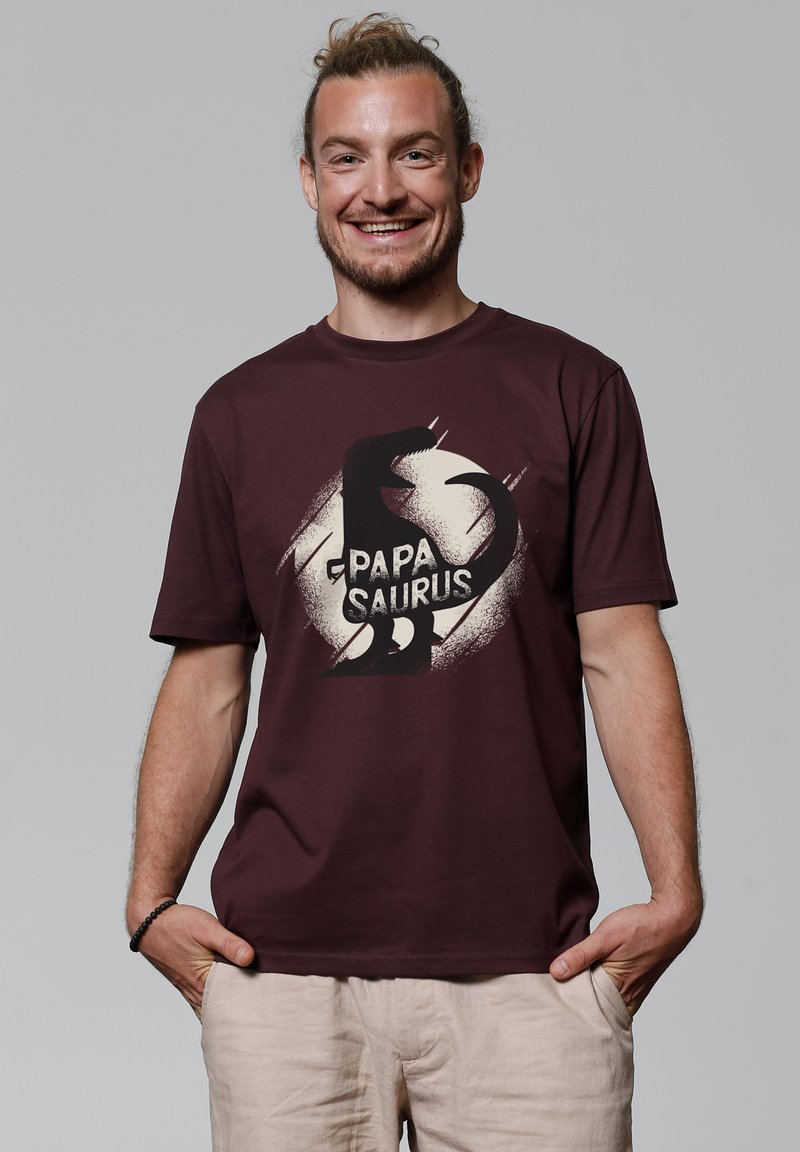 Bordeauxfarbenes Baumwoll-T-Shirt mit einem Dinosaurier-Grafik und dem Text "PAPA SAURUS" in Weiß. Kurzärmlig mit einem Rundhalsausschnitt.