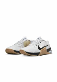 Ténis desportivos brancos com um swoosh preto da Nike, parte superior em malha, sobreposições texturizadas e sola de borracha com um padrão geométrico.