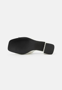 Black rubber sole with ridged texture, white midsole, and a square-shaped heel. The design features a smooth upper transition.