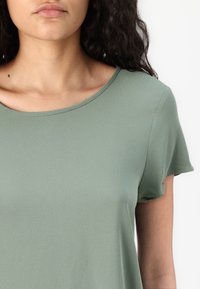 Short-sleeved, crew neck top in light green, made of a smooth fabric with a subtle texture and relaxed fit.