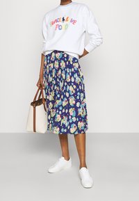 Bílá mikina se multicolorním nápisem "Peace Live Polo", zkombinovaná s modrou sukní s živými květinovými vzory. Bílé tenisky a kabelka.