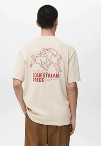 Cream-colored T-shirt with short sleeves, featuring a red line drawing of two horses and the text "EQUESTRIAN PRIDE" on the back.