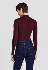 Top a maniche lunghe a costine color borgogna con collo alto, abbinato a jeans a vita alta blu scuro con tasche anteriori e posteriori.