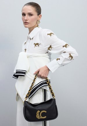 Bolso de cuero negro con cadena, adornado con un leopardo dorado y un embellish de "C". Camisa blanca con patrones de leopardo dorados, de corte elegante.