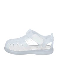 Sandalias blancas translúcidas con punta cerrada y lados abiertos, que cuentan con una correa de Velcro y un diseño ranurado para ventilación.