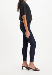 Camiseta negra de manga corta combinada con jeans ajustados azul oscuro y sandalias de tacón negras, enfatizando el diseño entallado y la textura del denim.