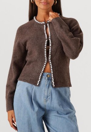 Brauner gestrickter Cardigan mit Perlenverzierungen entlang der Öffnung, rundem Halsausschnitt und langen Ärmeln, kombiniert mit hellblauen hochtaillierten Jeans.
