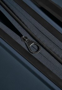 Gros plan d'une fermeture éclair noire et bleue partiellement ouverte sur un tissu texturé avec des bords en caoutchouc noir.
