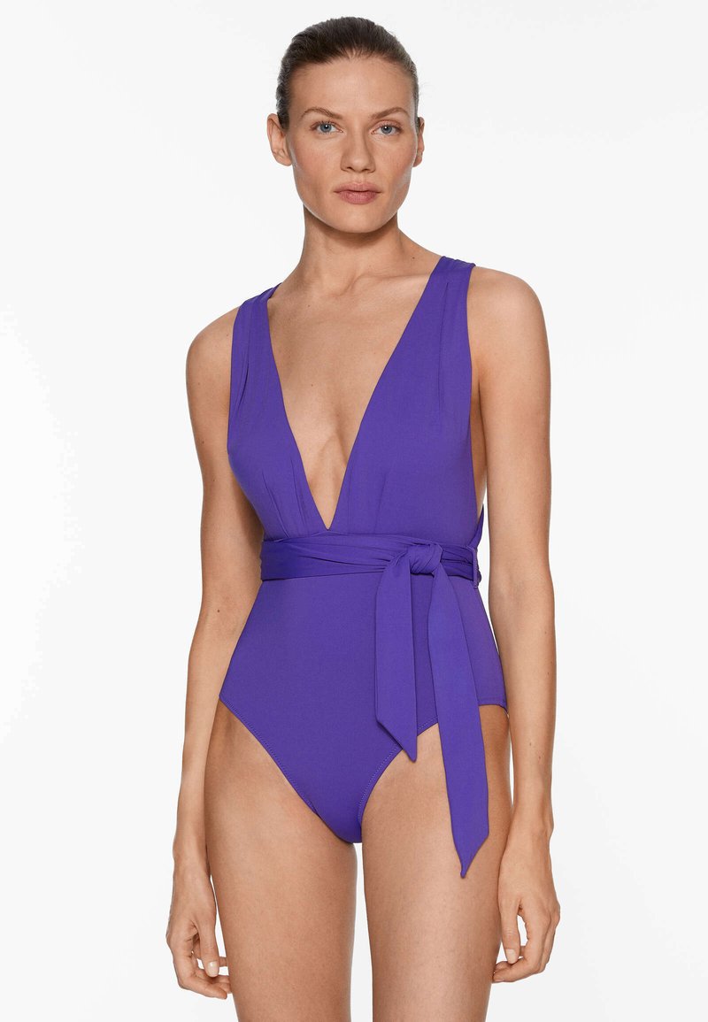 Maillot de bain une pièce violet avec un décolleté en V profond, des bretelles larges et un détail à nouer à la taille. Tissu lisse avec une silhouette ajustée.