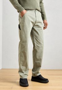 Lys grønne cargo bukser med sidelomme, lavet af bomuldsstof; har en løs pasform med lige ben, parret med sorte slip-on sko.