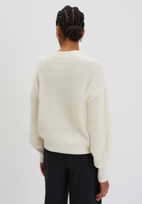 Maglione a maglia grossa con un fit rilassato, maniche ampie e orlo a costine. Tessuto testurizzato con un motivo di trama aperta. Pantaloni neri.