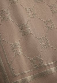 Textiel in gedempt bruin met een delicate bloemmotief en verhoogde borduursels. Decoratieve rand benadrukt het ontwerp. Zachte textuur.