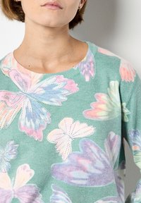 Zielony sweter z wzorem motyli w pastelowych kolorach, ozdobiony dekoracyjnymi kryształkami, z okrągłym dekoltem. Miękki, teksturowany materiał.