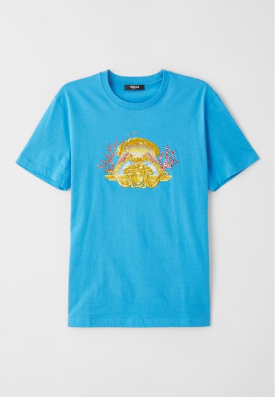 Camiseta de algodão azul com um design gráfico em dourado e coral, apresentando um motivo clássico no centro. Manga curta e decote redondo.