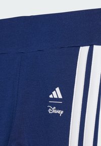 Pantalones deportivos azul marino con diseño de tres rayas blancas, logo de Adidas y marca de Disney en una cintura de tela texturizada.
