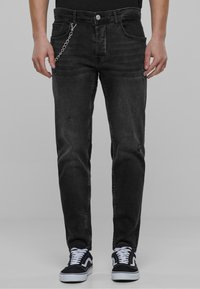 Musta farkut slim fit -mallilla, joissa on näkyvä ketju koristeena, hienovarainen kulutus, ja perinteinen viisi taskua -design. Yhdistetty mustiin tennareihin.