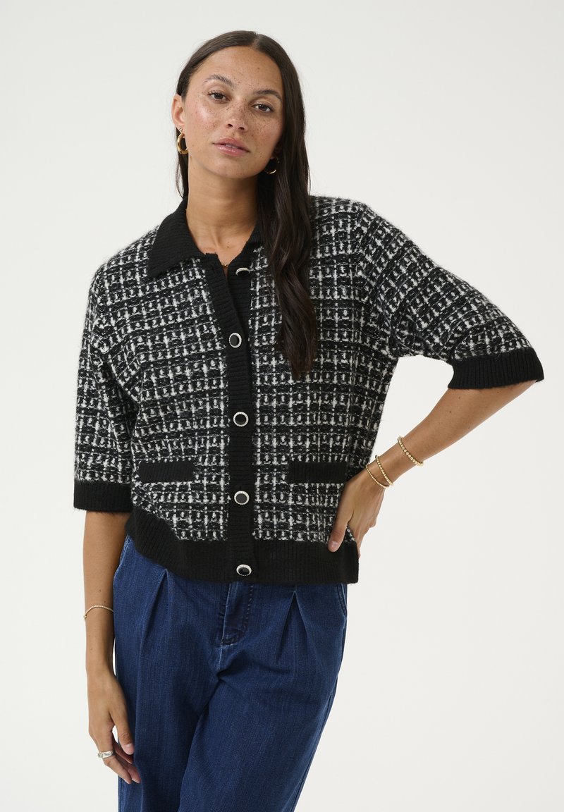 Black and white textured cardigan with a collar, short sleeves, button closure, and two patch pockets. Knit fabric pattern is checkered.