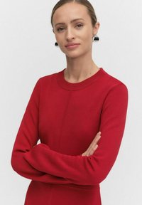 Rode gebreide jurk met lange mouwen, ronde halslijn en een aansluitende silhouet. Heeft een gestructureerde stof en subtiele naaddetails aan de voorkant.